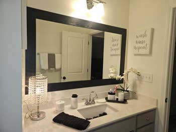 A well-lit bath vanity with mirror, decorative lamp, and substance partition creation saying