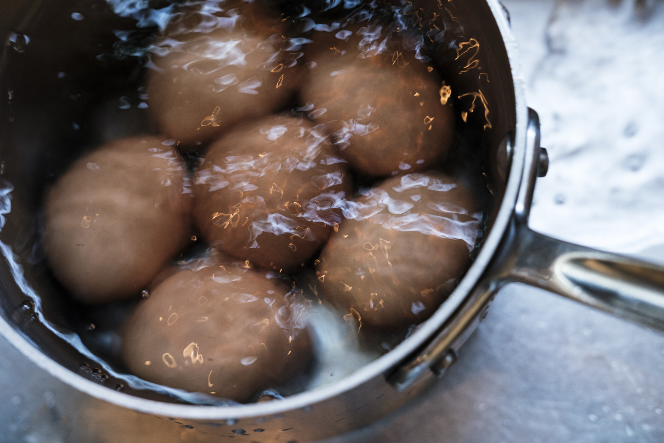 Pot with boiling eggs, steam rising, close-up view