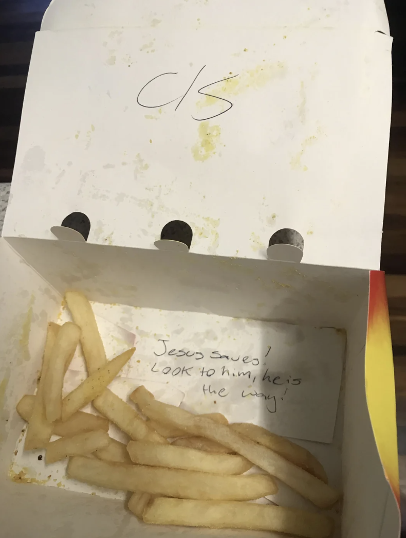 Open fast-food container with fries and a handwritten message about Jesus inside the lid