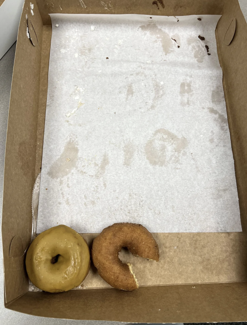 An almost empty doughnut box with one whole and one half-eaten doughnut left