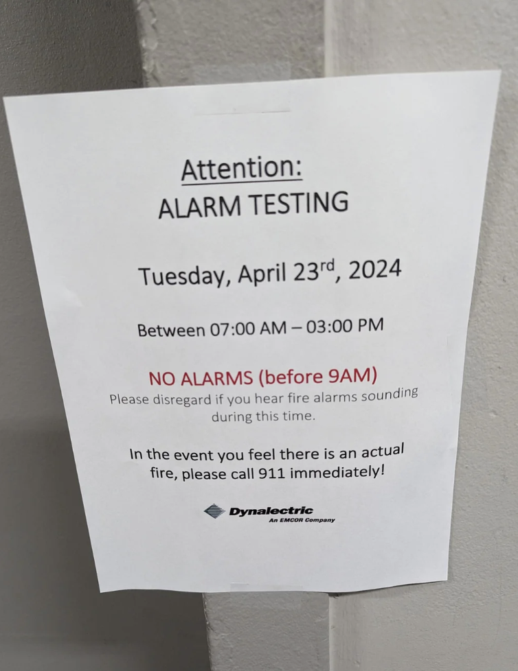 Sign on wall announcing alarm testing on Tuesday, April 23rd, 2024 with instructions and emergency contact information