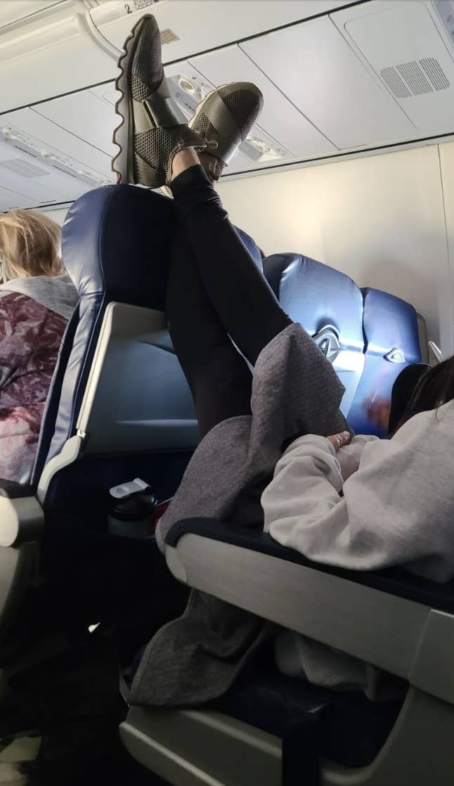 Passenger with feet resting on airplane seatback, another person seated adjacent