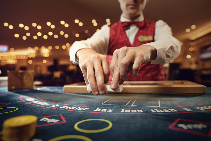 Casino dealer in uniform shuffling cards at a blackjack table with chips in the foreground