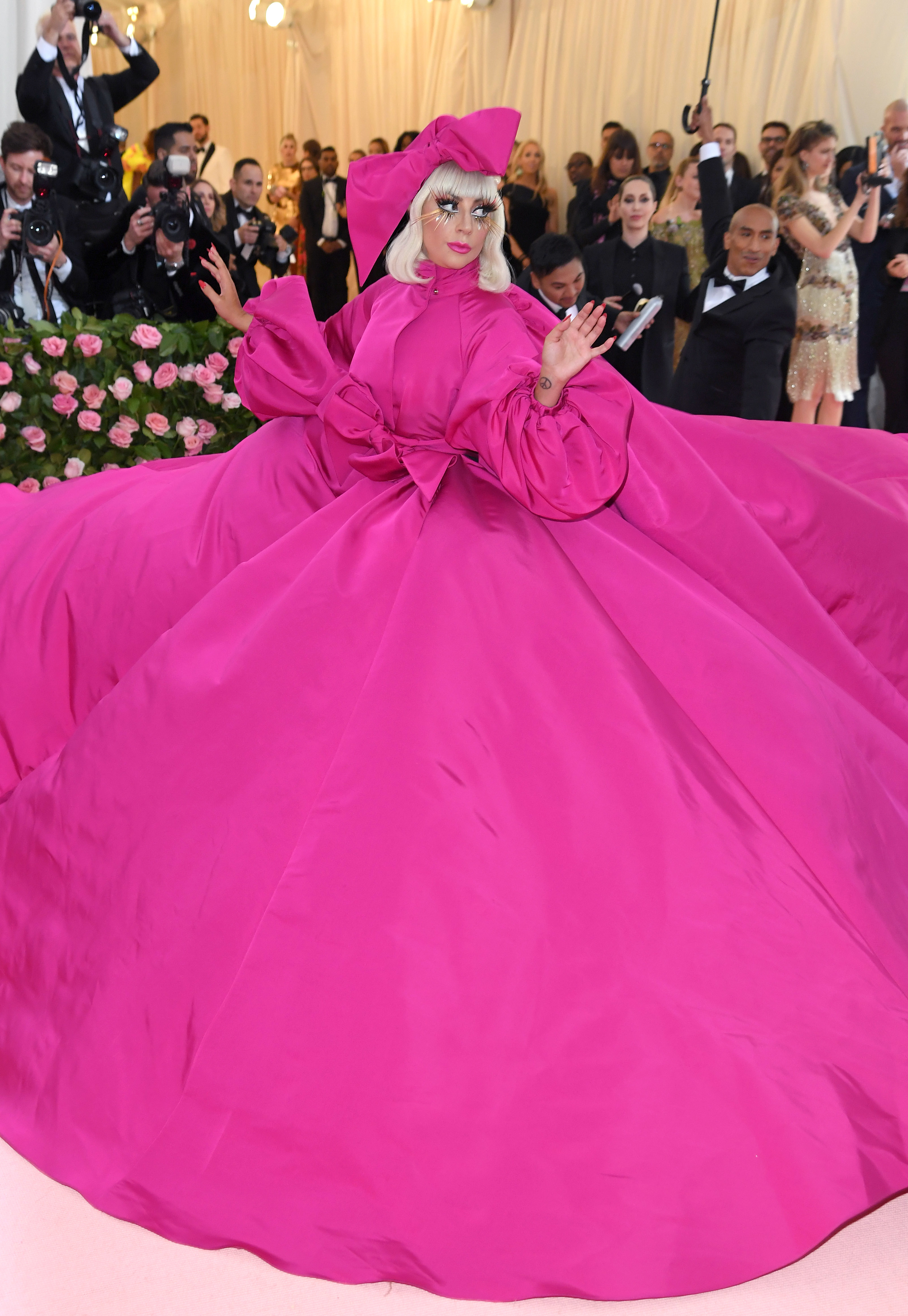 Lady Gaga en la gala Met con un deslumbrante vestido abultado y lazo grande, y una cofia a juego. Fotógrafos al fondo