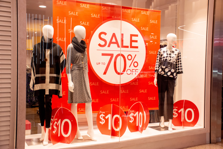 Storefront window displaying mannequins with signs advertising a sale up to 70% off and items for $10