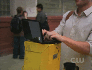 Person hastily typing on a laptop placed on a yellow trash can