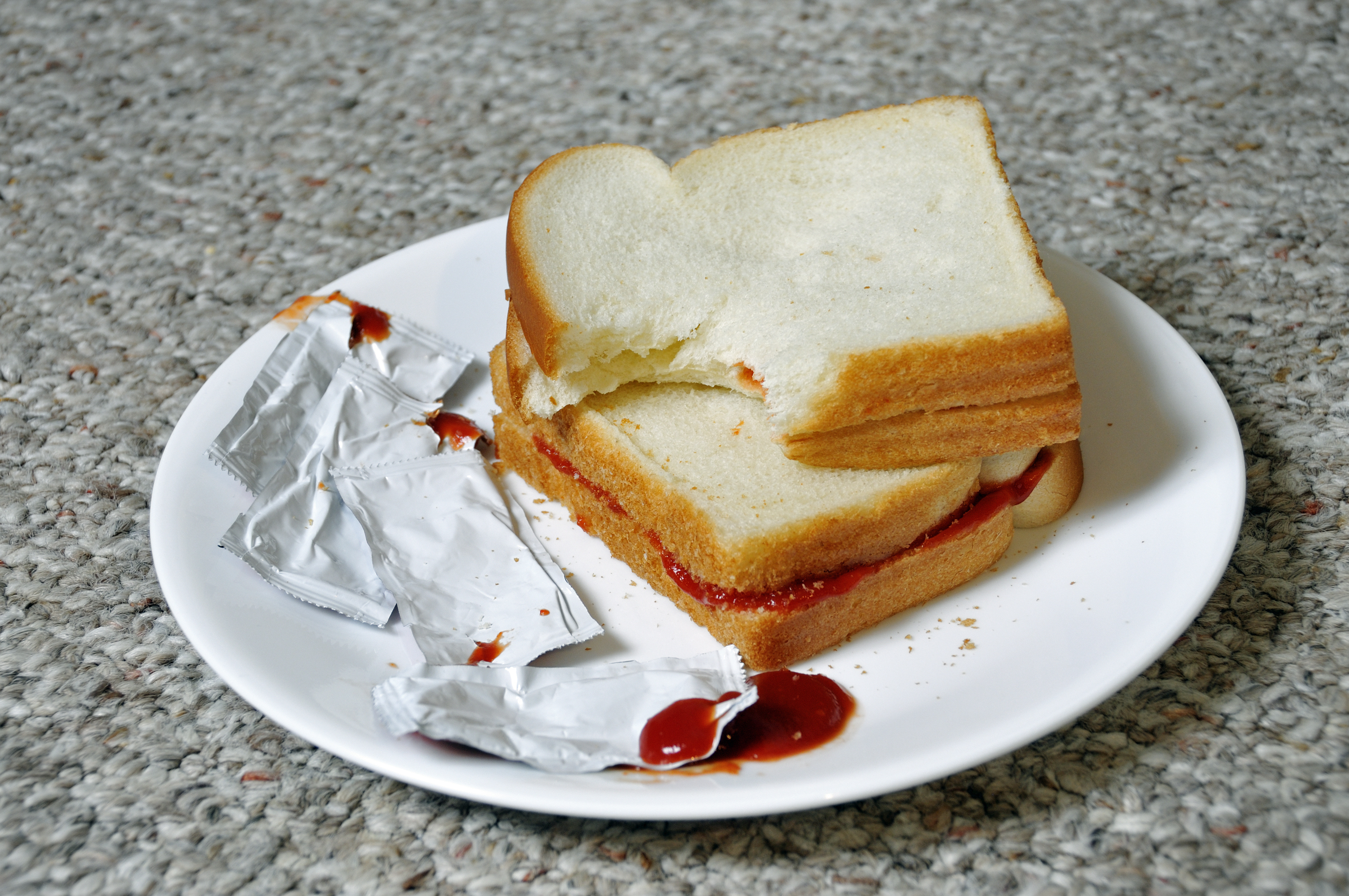 A half-eaten sandwich with ketchup and an empty condiment packet on a white plate