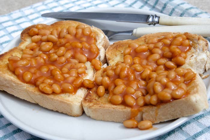 Two slices of toast with baked beans on a plate beside a knife and fork