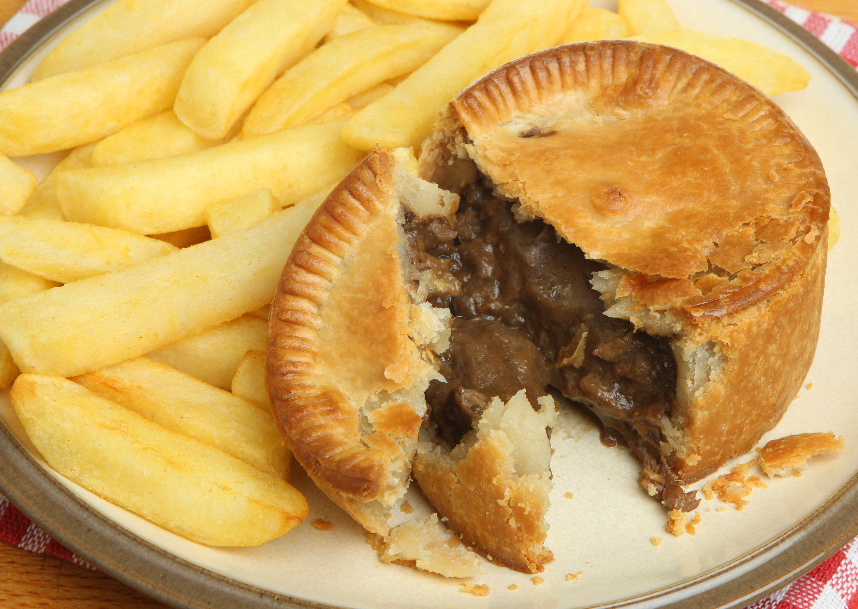 A meat pie with a bite taken out, on a plate with French fries