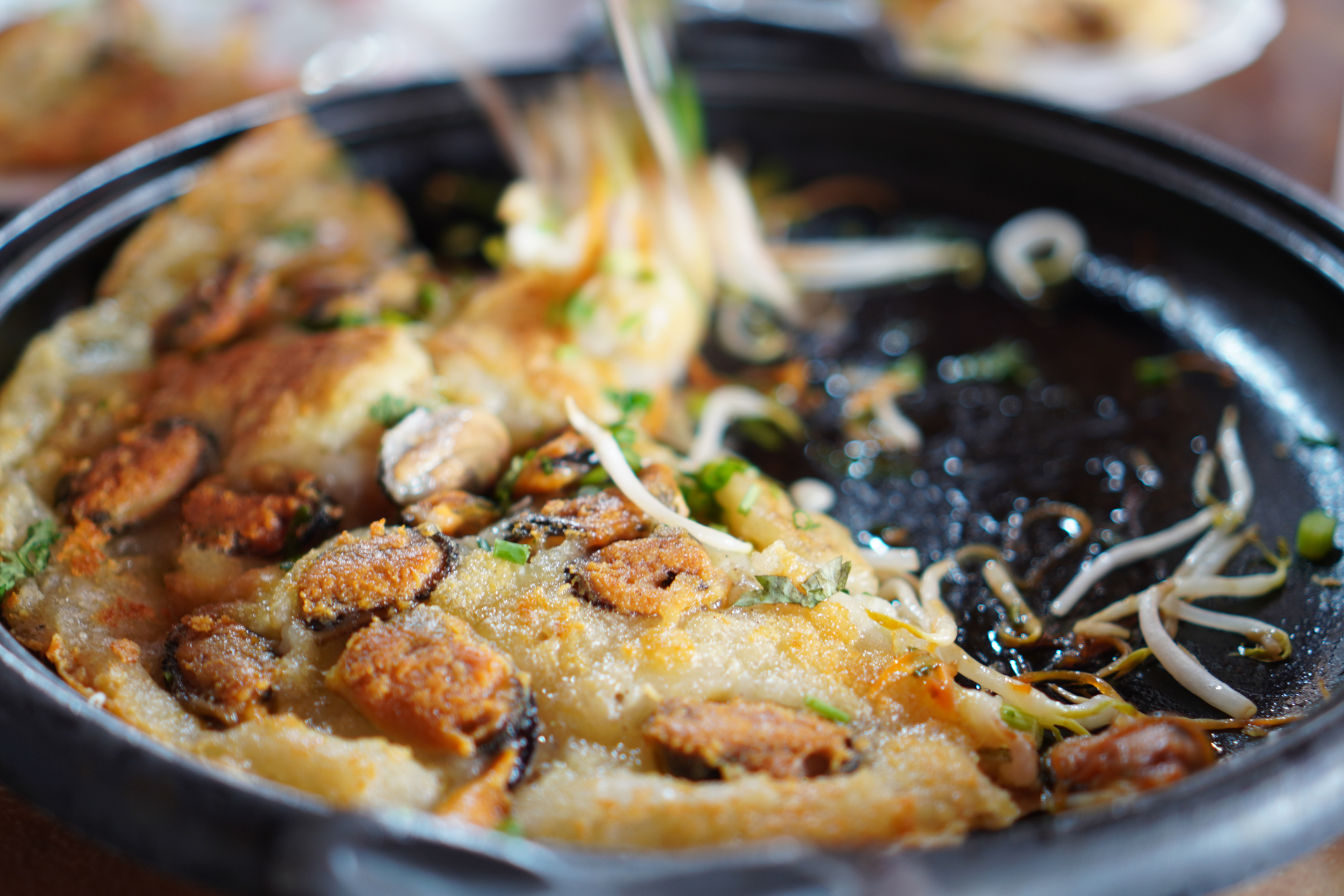 Sizzling plate of Korean seafood pancake with side toppings ready to be served
