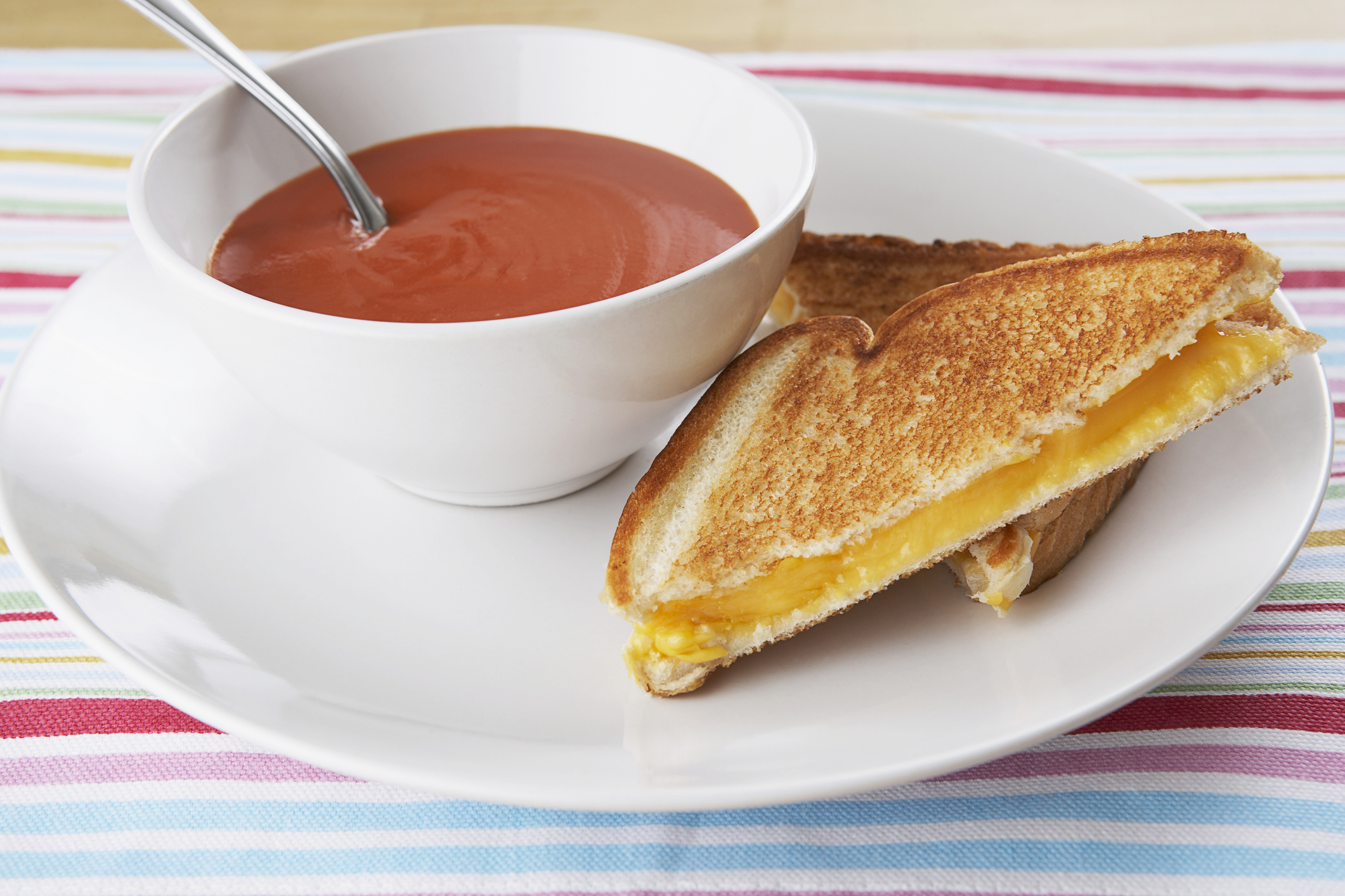 Bowl of tomato soup with a grilled cheese sandwich on a striped placemat