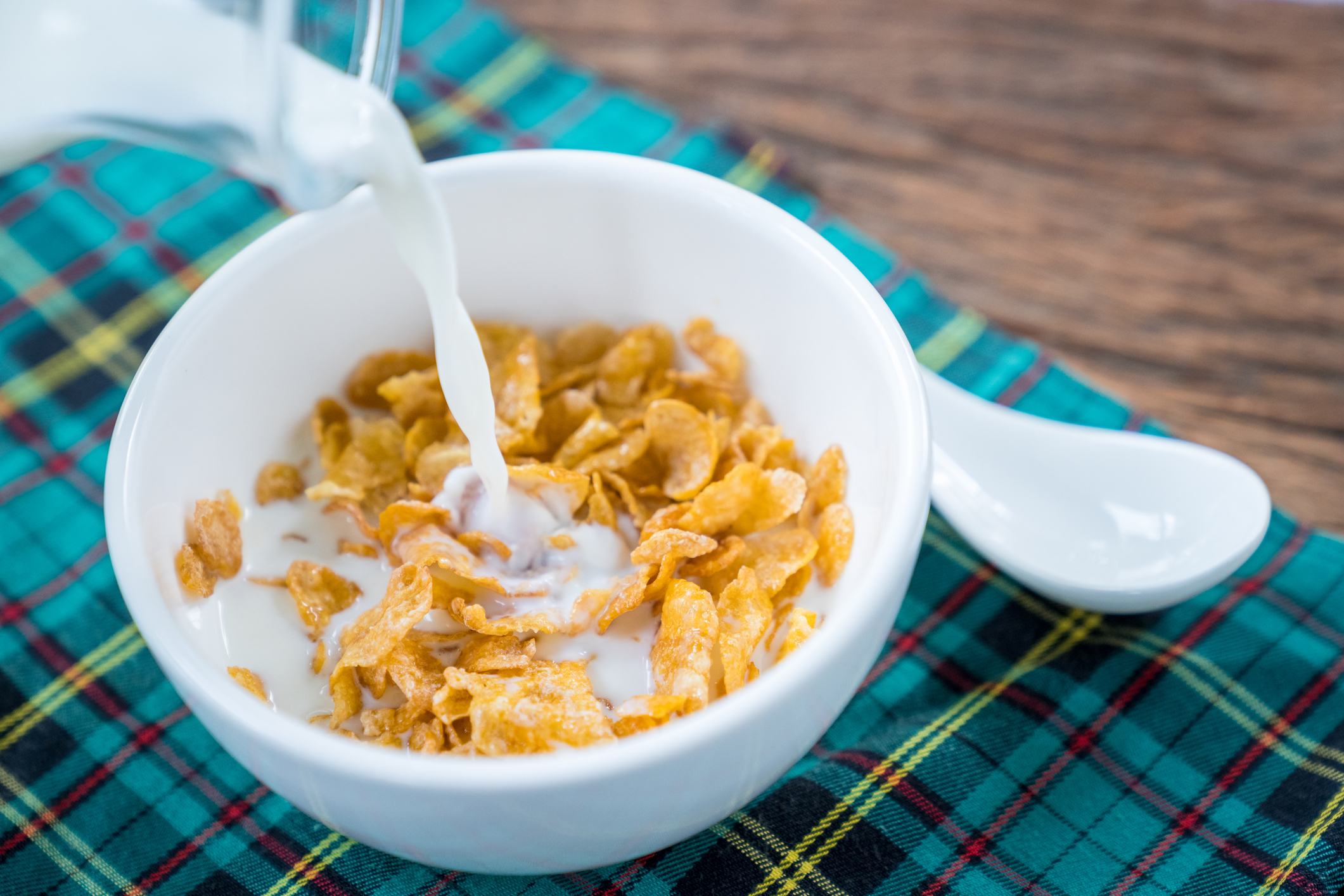 Milk being poured into a bowl of cornflakes on a plaid cloth