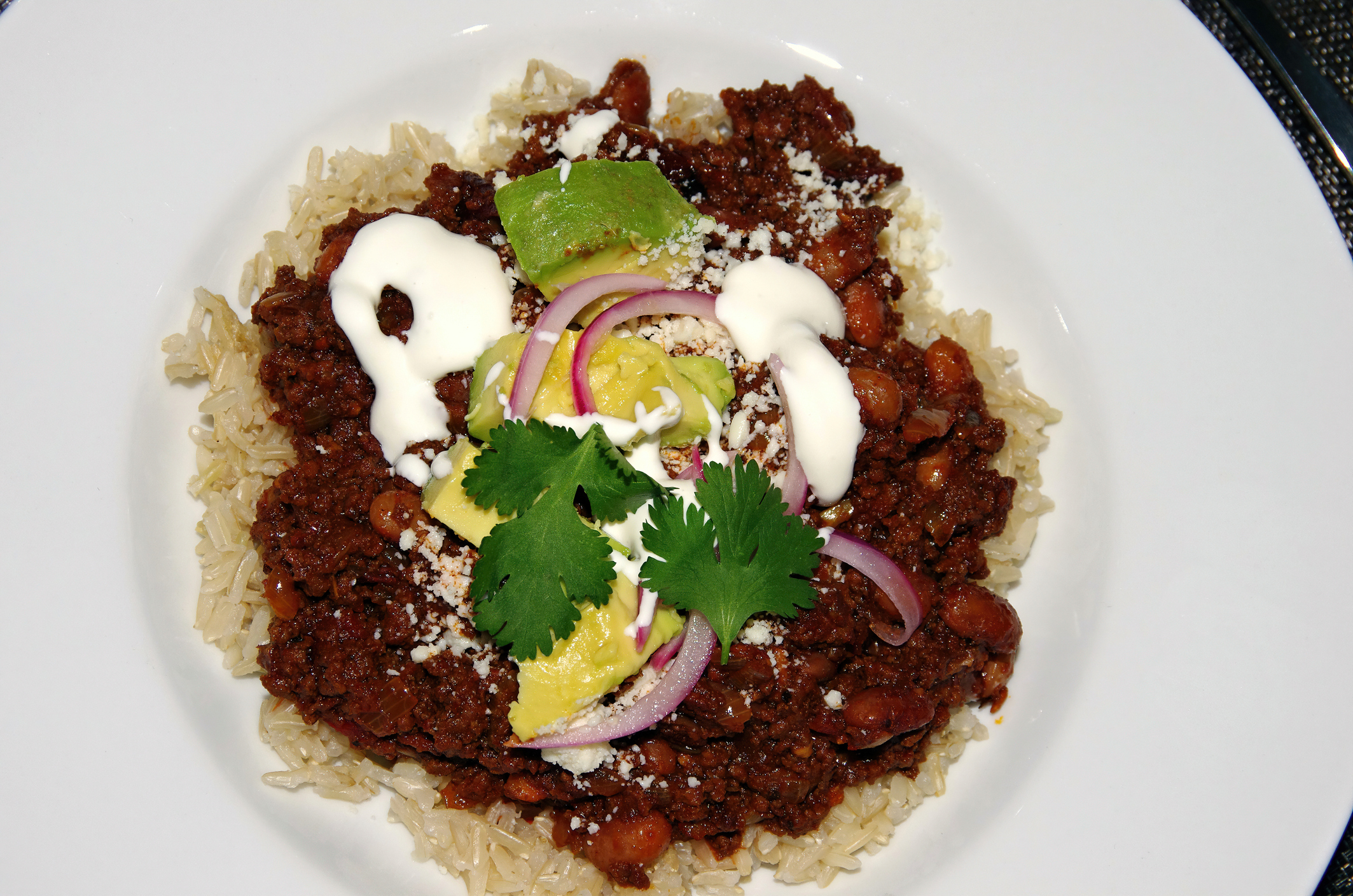 Plate containing rice and beans topped with ground meat, sour cream, lime wedges, onion, and cilantro