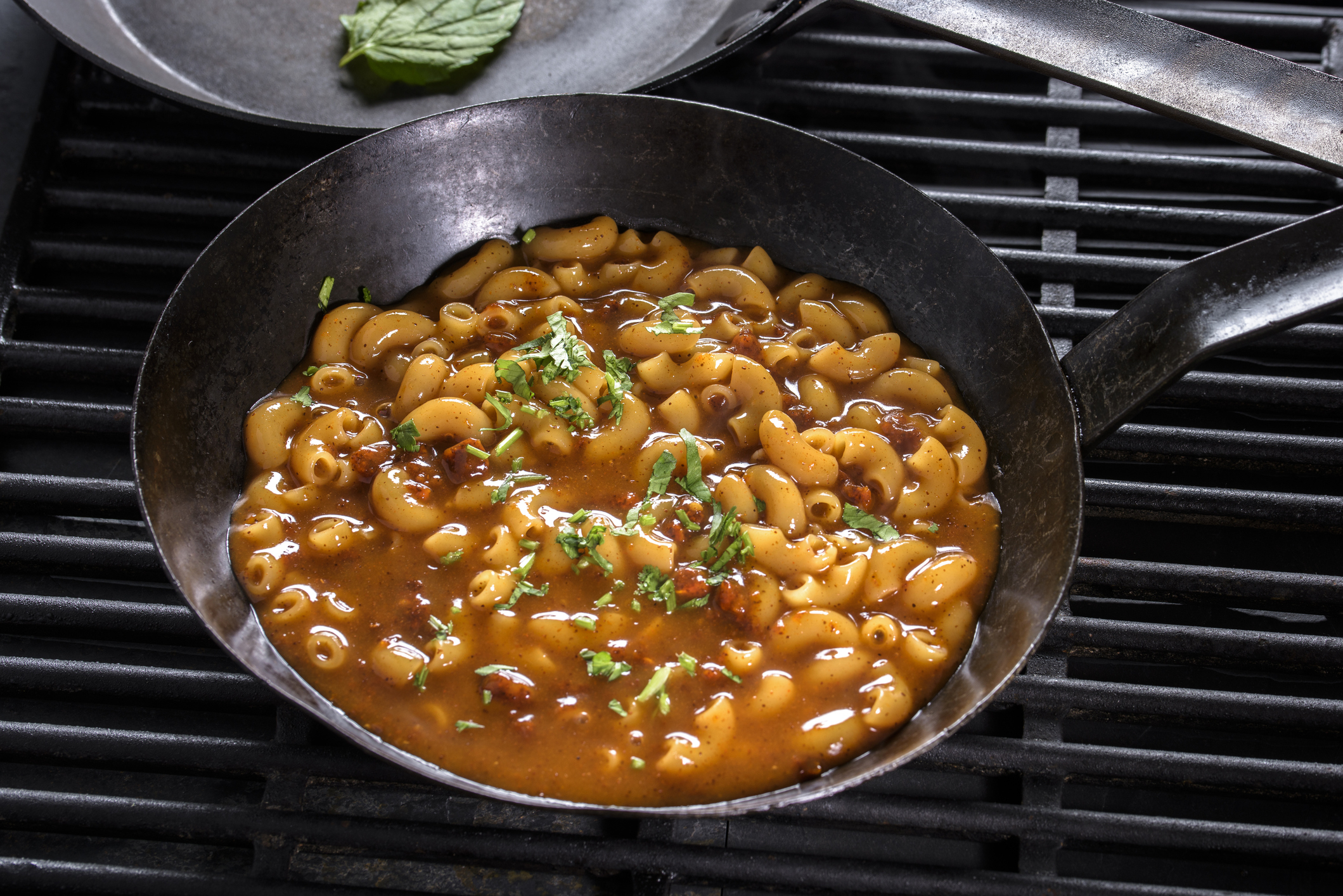 A skillet of baked beans garnished with herbs on a stove grille