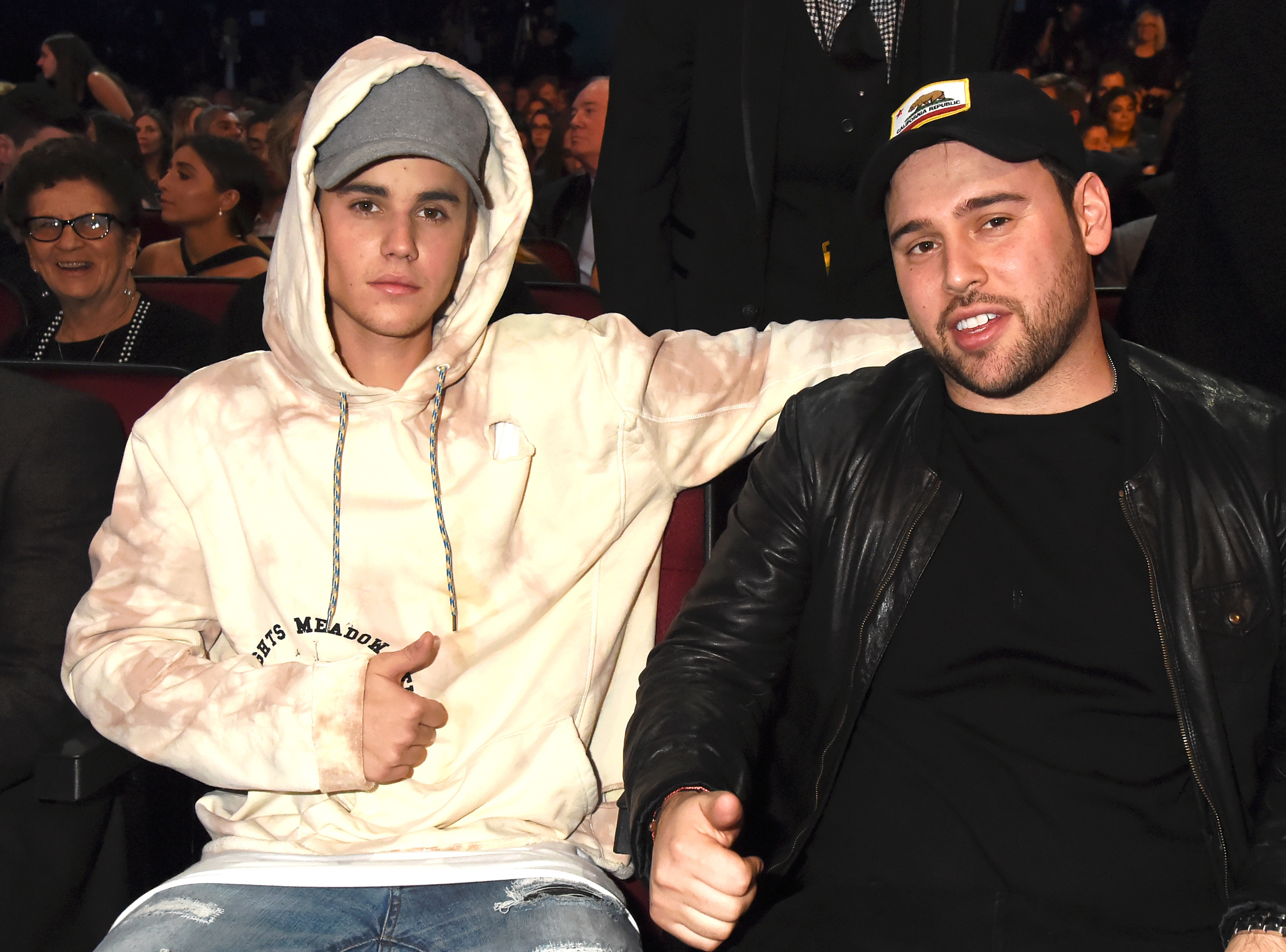 Justin Bieber in a white hoodie seated next to Scooter Braun in a black leather jacket
