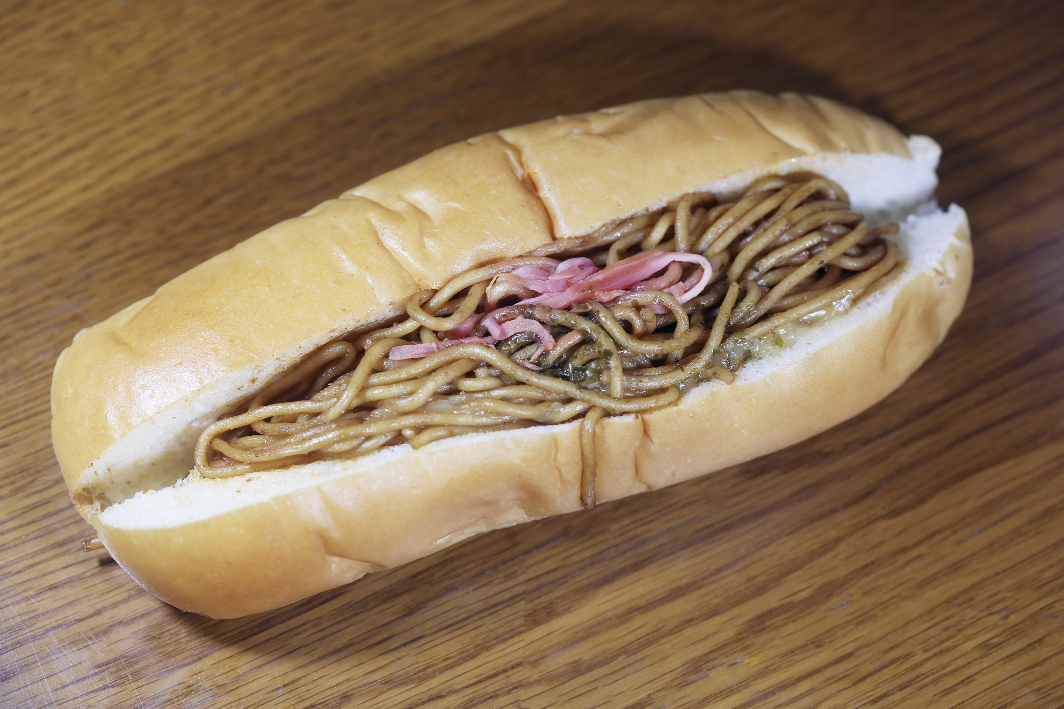 A sandwich filled with noodles and topped with pickled ginger, resting on a wooden surface