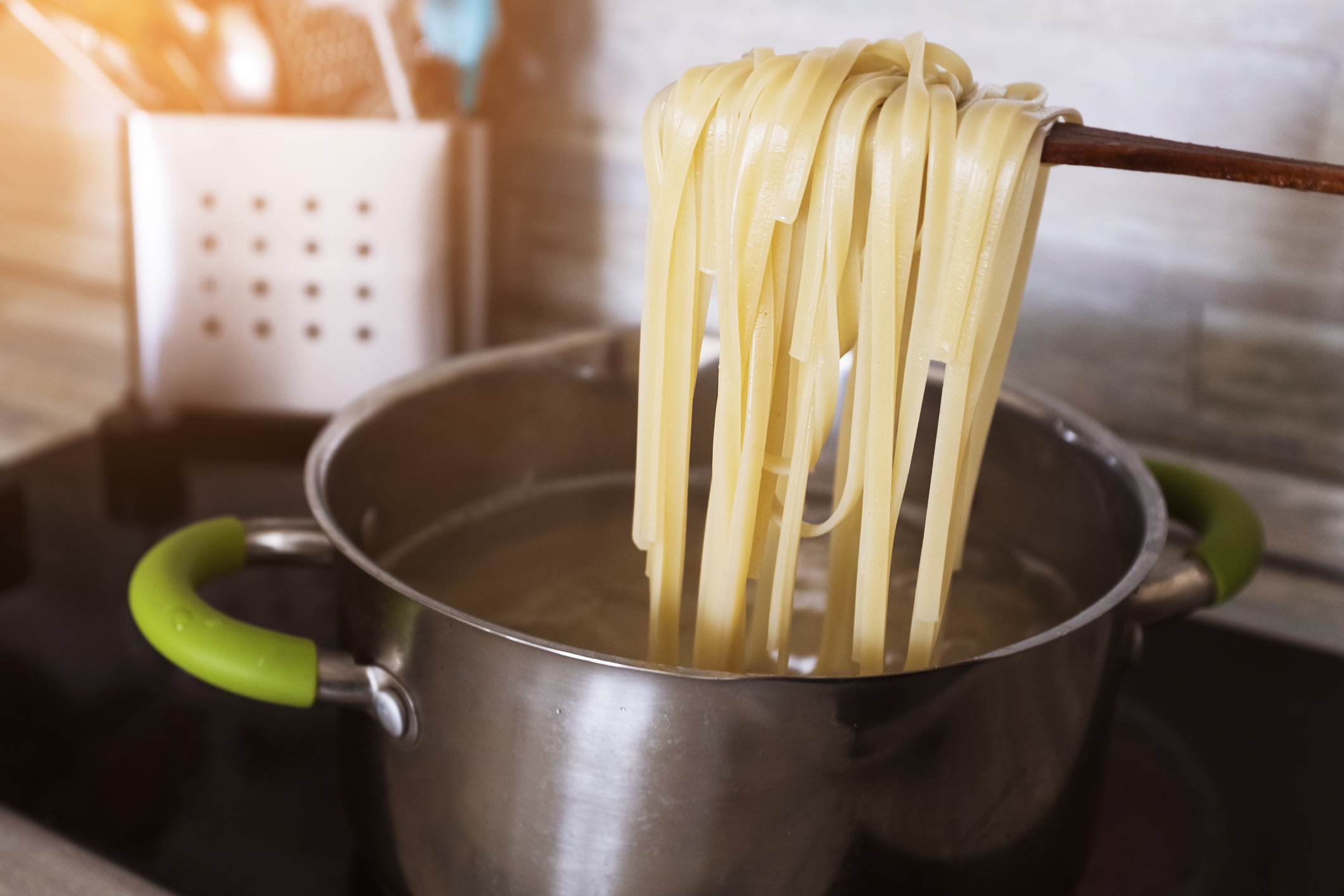 Cooked spaghetti lifted from a pot with tongs, steam rising, beside a grater