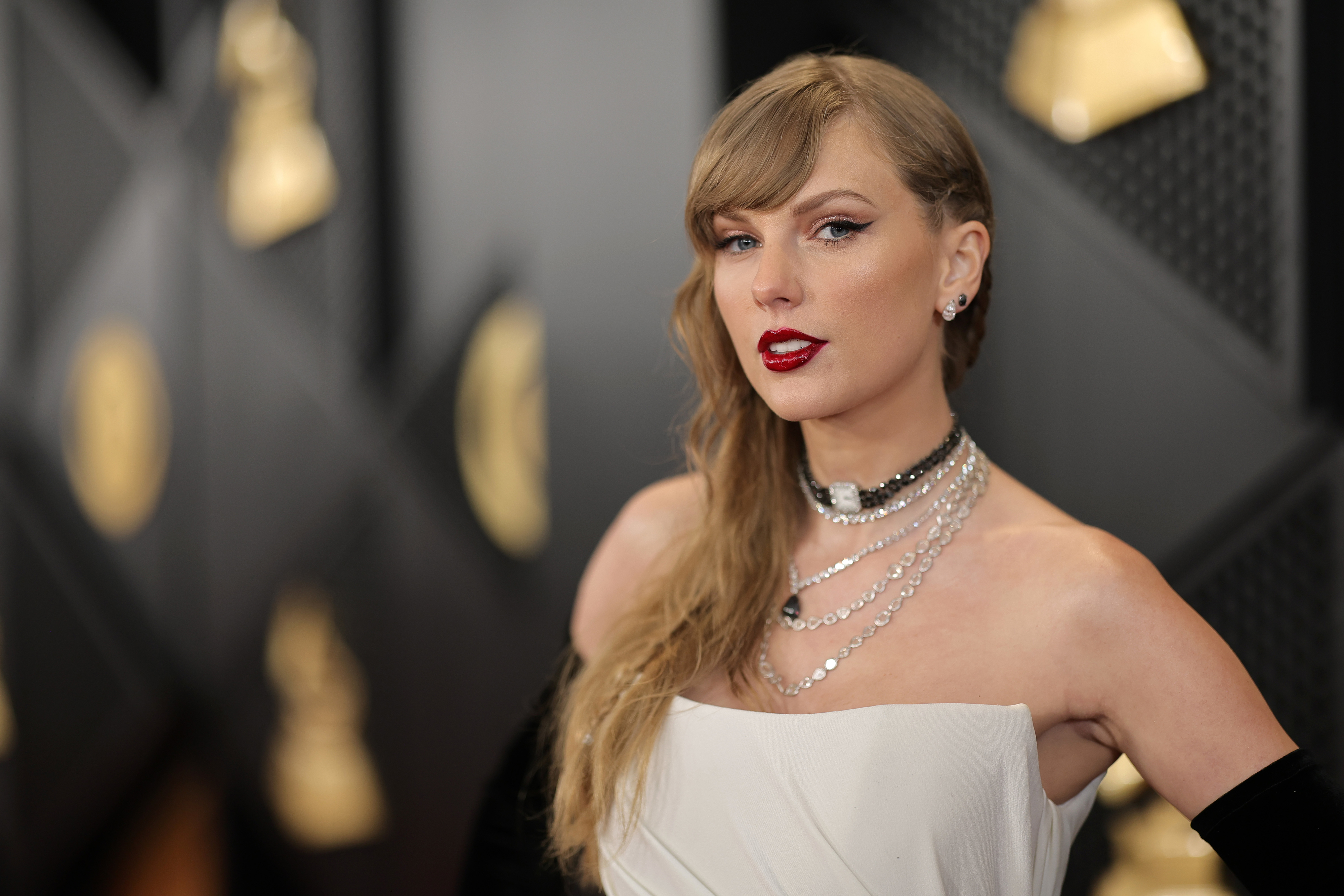 Taylor Swift in an elegant off-shoulder gown with a layered necklace, striking a pose