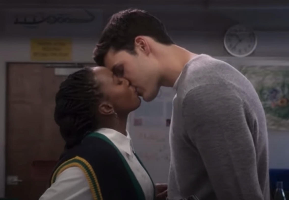 Two characters sharing a kiss, the setting appears to be a school classroom