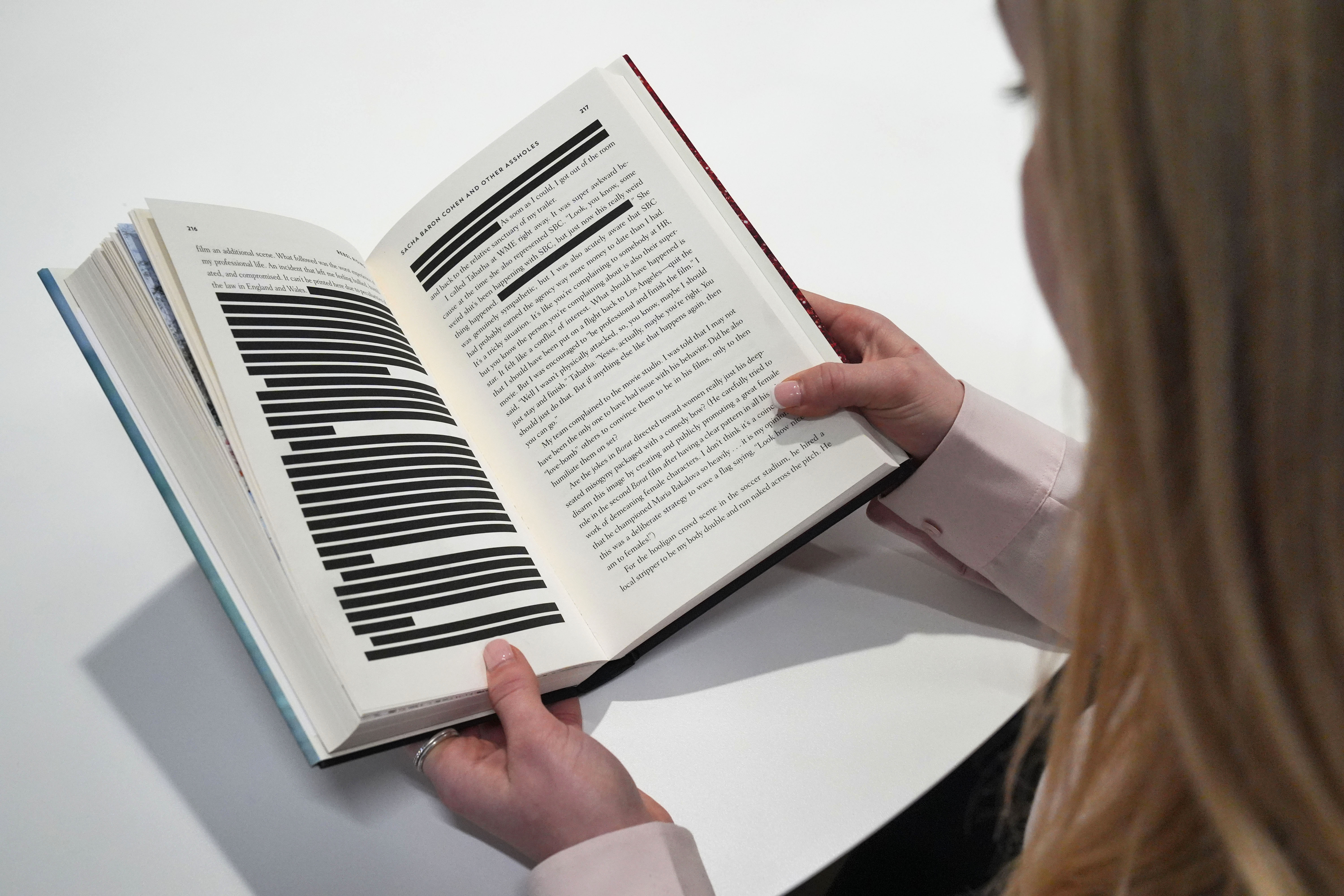 An individual holding a book with redacted text on visible pages