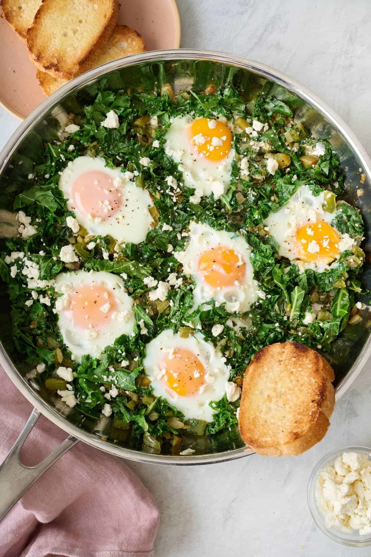 Skillet with sautéed greens and four sunny-side-up eggs, served with toast on the side