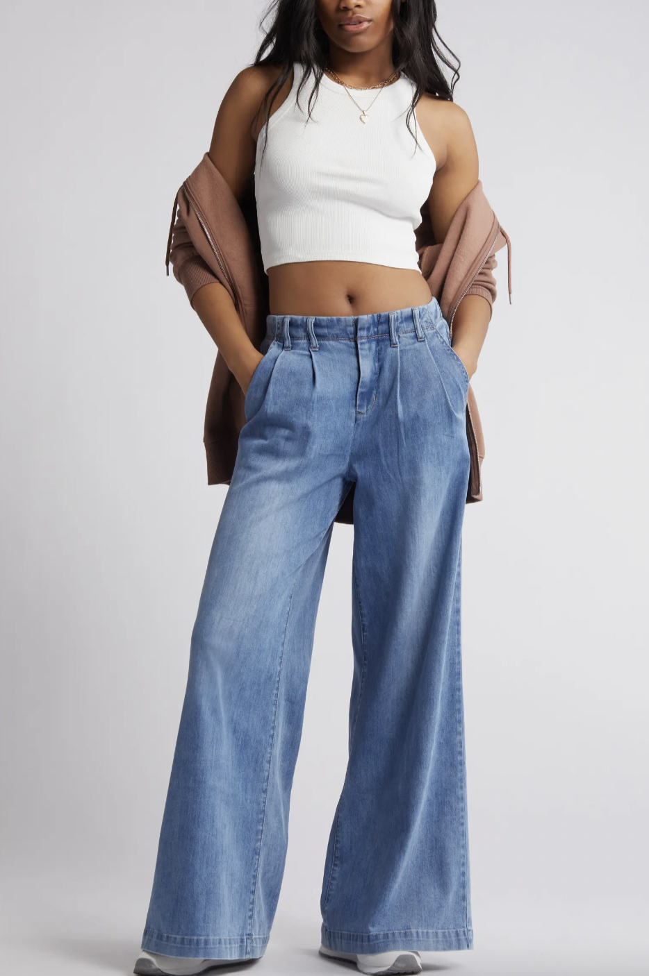 Woman in white crop top and wide-leg jeans, holding a jacket over her shoulder