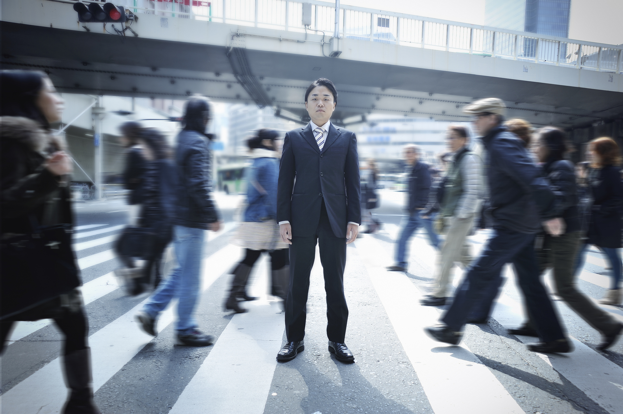 Man in suit standing still while blurred figures walk around him