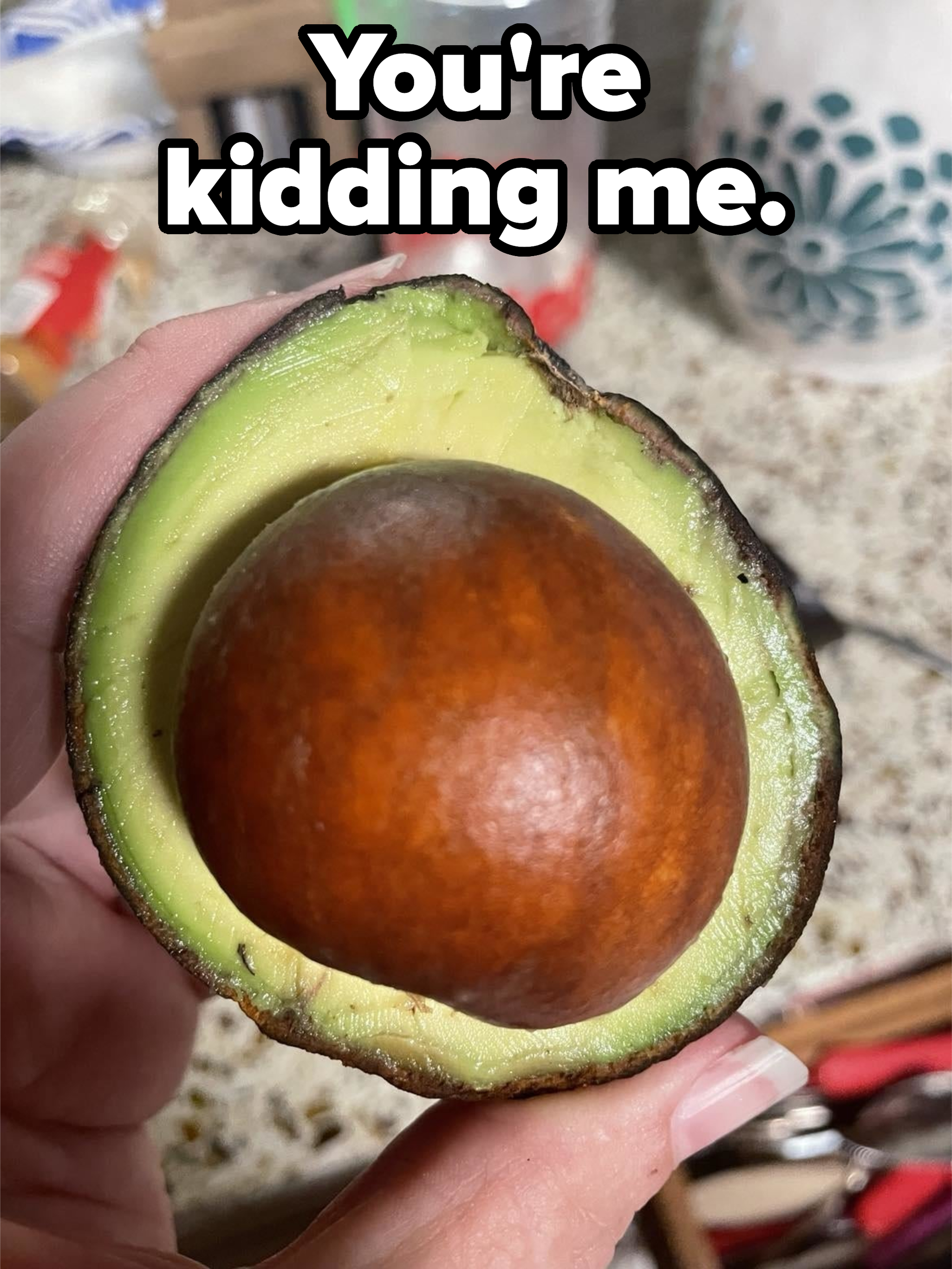 Person holding a ripe avocado cut in half, showcasing the seed and green flesh