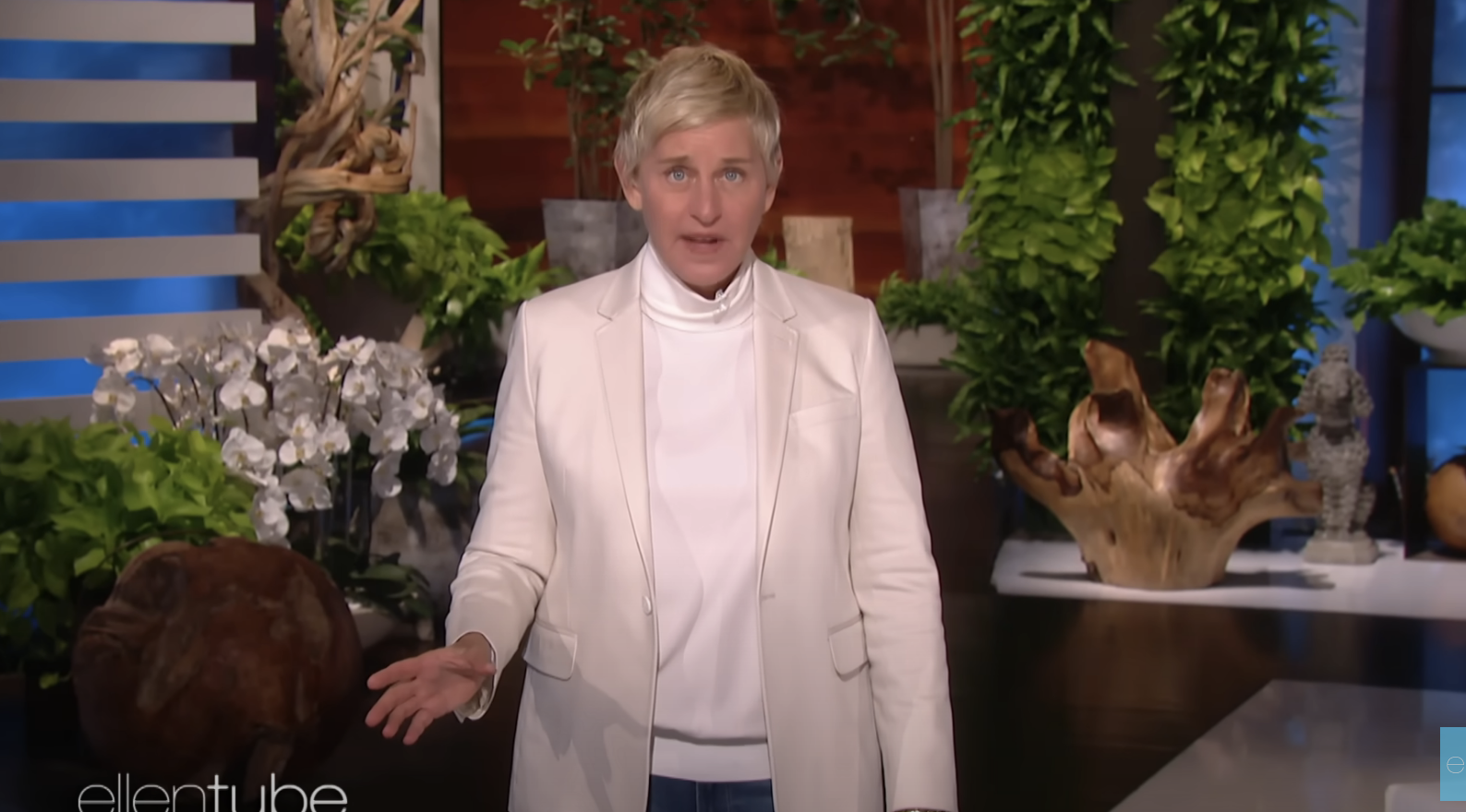 Ellen DeGeneres in a white suit jacket and turtleneck on her talk show set