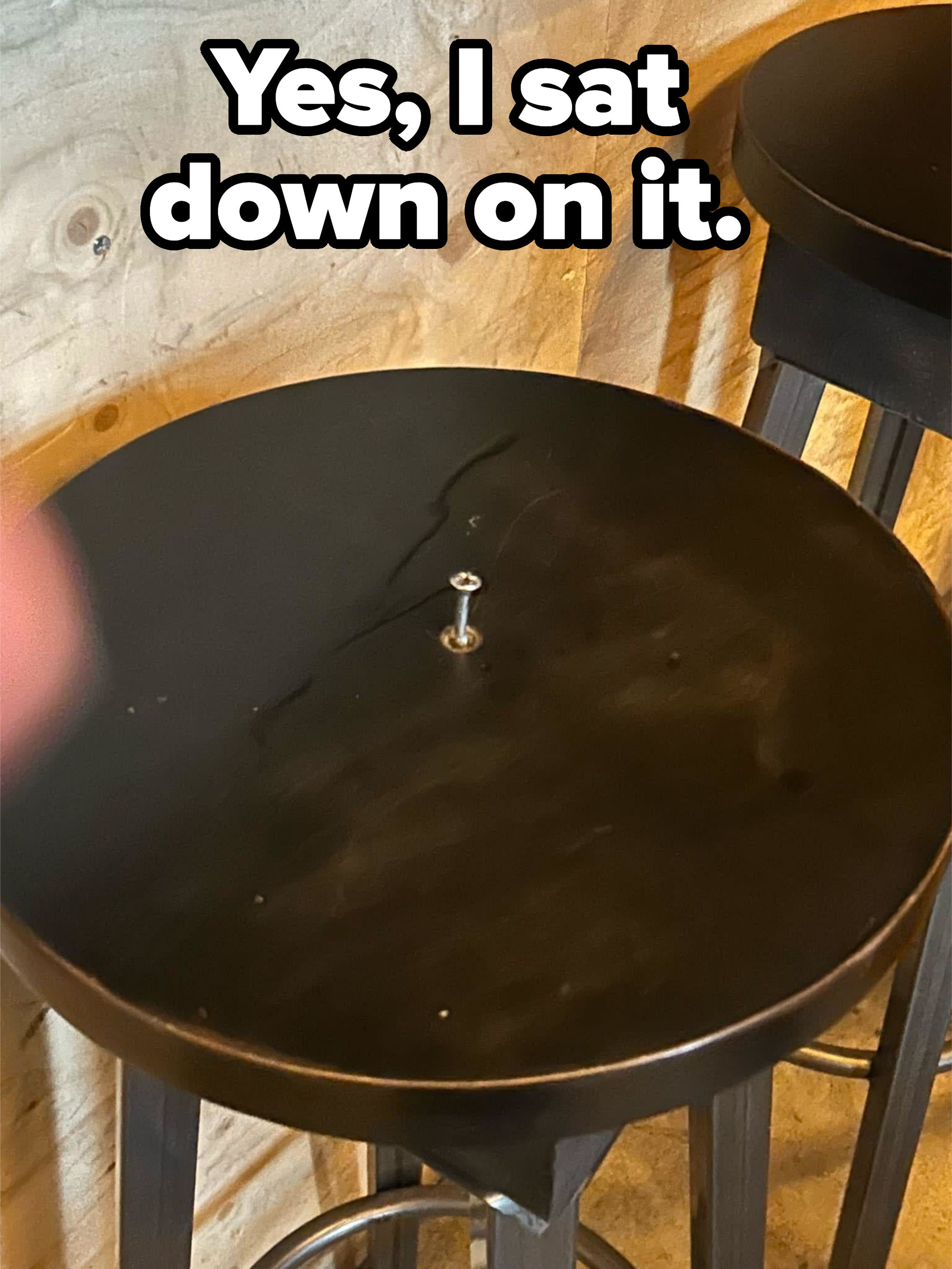 A single screw lies in the center of an empty round stool with a wooden background