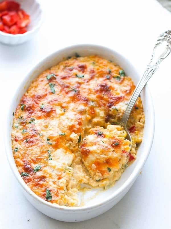 A baked casserole with melted cheese on top, served in a white dish with a spoon
