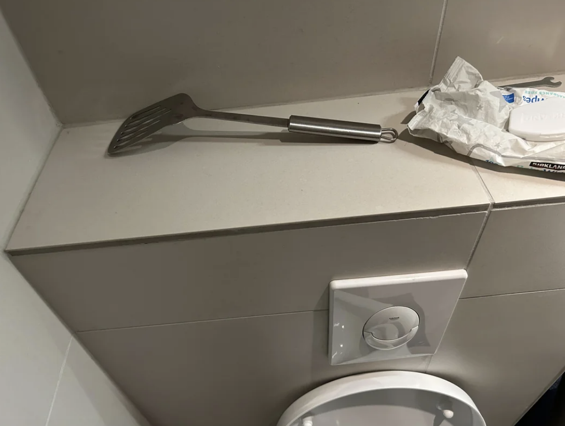 A spatula and a crumpled tissue rest on a bathroom counter beside a toilet paper holder