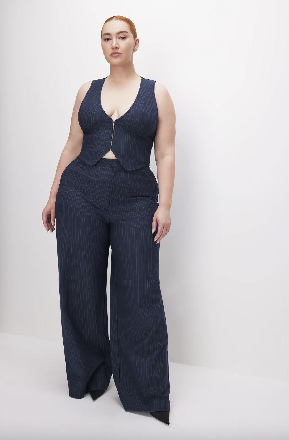 Woman in a stylish pinstripe jumpsuit, posing with hands on hips