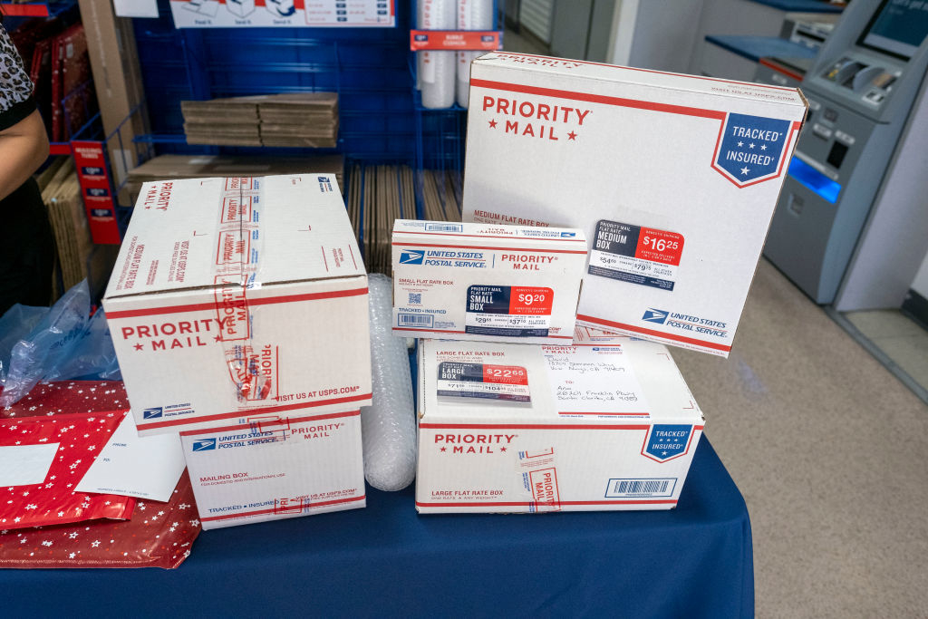 A pile of Priority Mail boxes with various postage rates on a counter