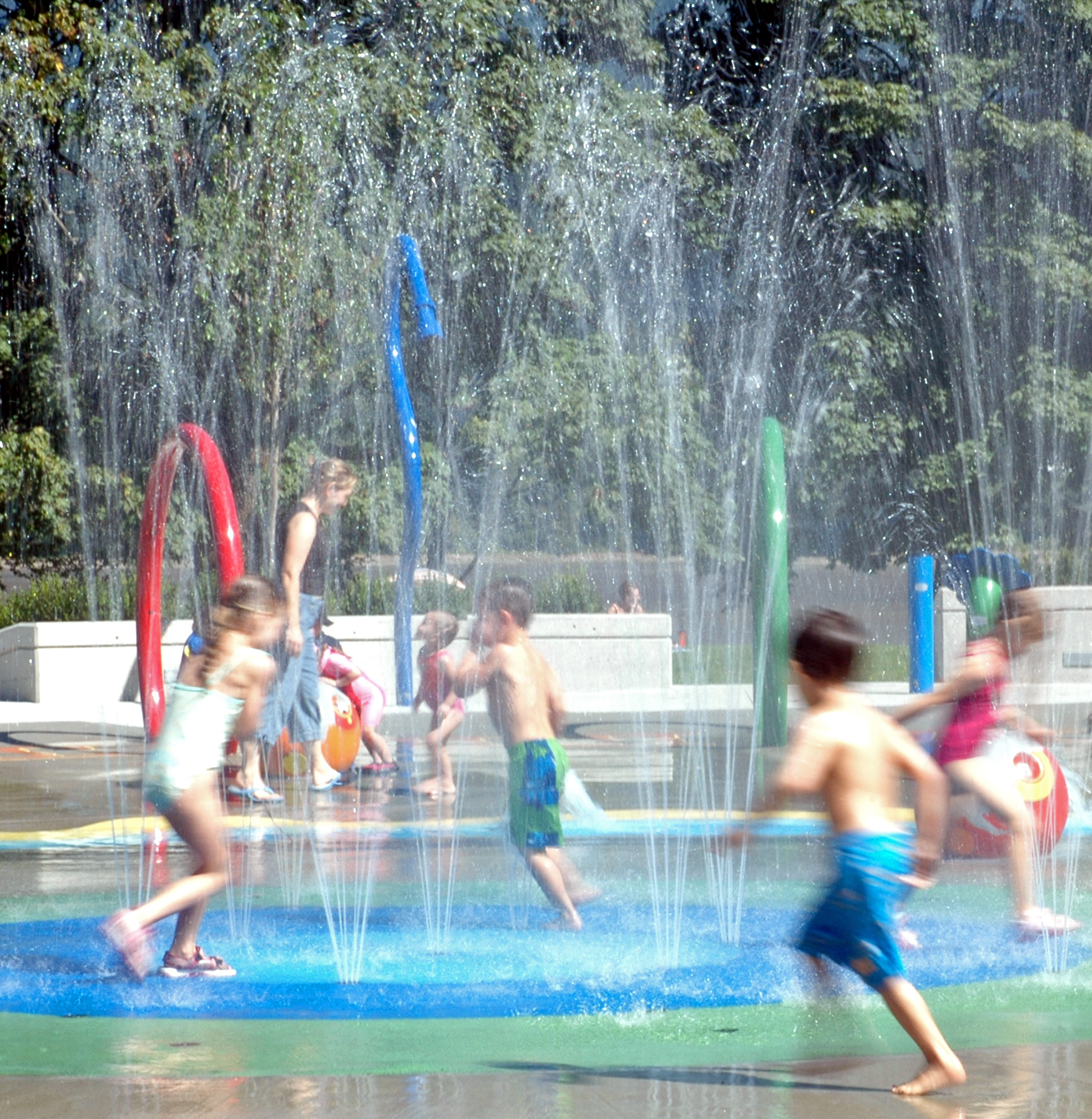 Children play in a splash pad with water streams and colorful structures