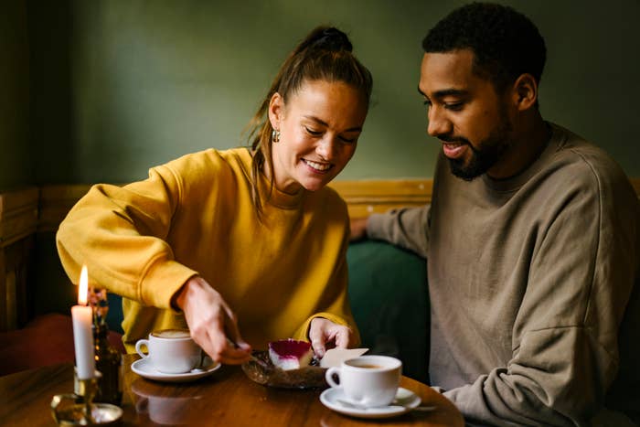 Two people smiling, sharing dessert in a cozy setting with coffee