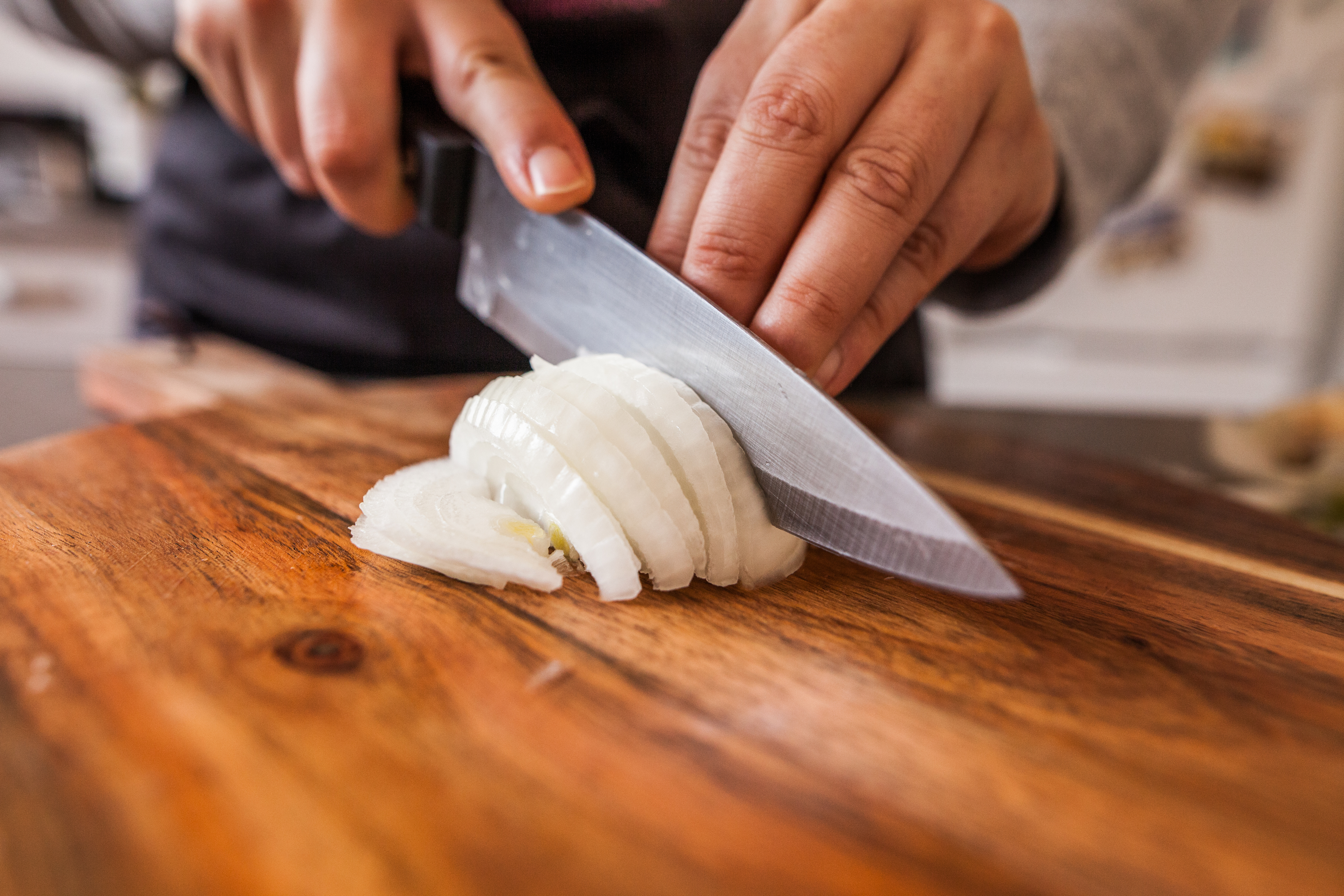 Person slicing an onion on a wooden board, demonstrating food prep skills essential in culinary jobs
