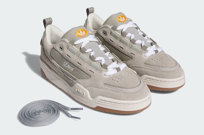 Pair of beige sneakers with white laces, extra grey laces on the side, and orange brand logos