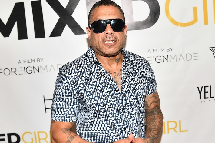 Man in patterned short-sleeved shirt and sunglasses posing at event with 'MIXED GIRL' backdrop