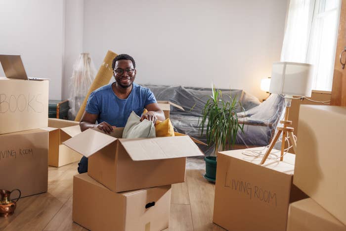 Man smiling sitting with cardboard boxes in a new home, labeled for different rooms