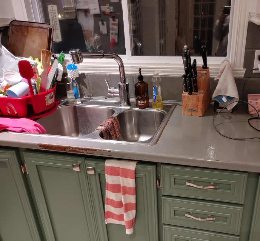 A tidy kitchen sink with cleaning tools, soap dispensers, and a striped towel on green cabinets