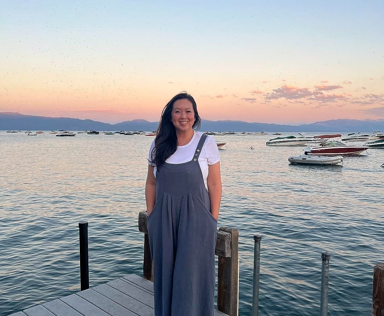 reviewer on a pier in lake tahoe wearing the gray-blue jumpsuit with boats and sunset in the background