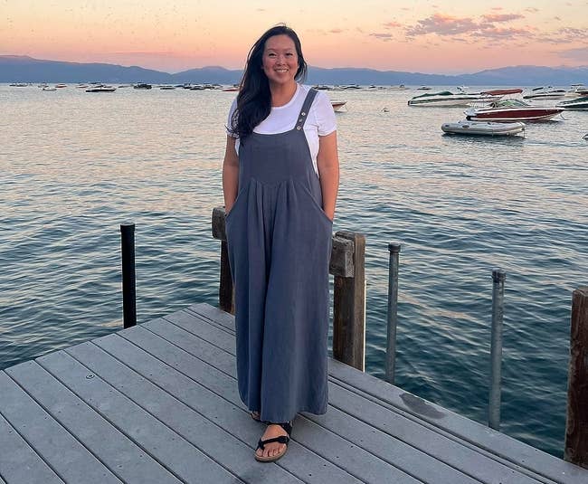 reviewer connected a pier successful water tahoe wearing the gray-blue jumpsuit with boats and sunset successful the background