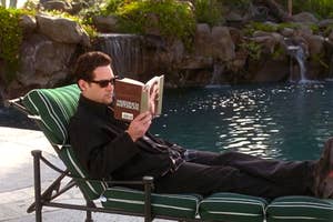 Paul Rudd lounges on a chair by a pond, reading "Friedrich Nietzsche" book, dressed in casual black attire in the movie "Clueless."