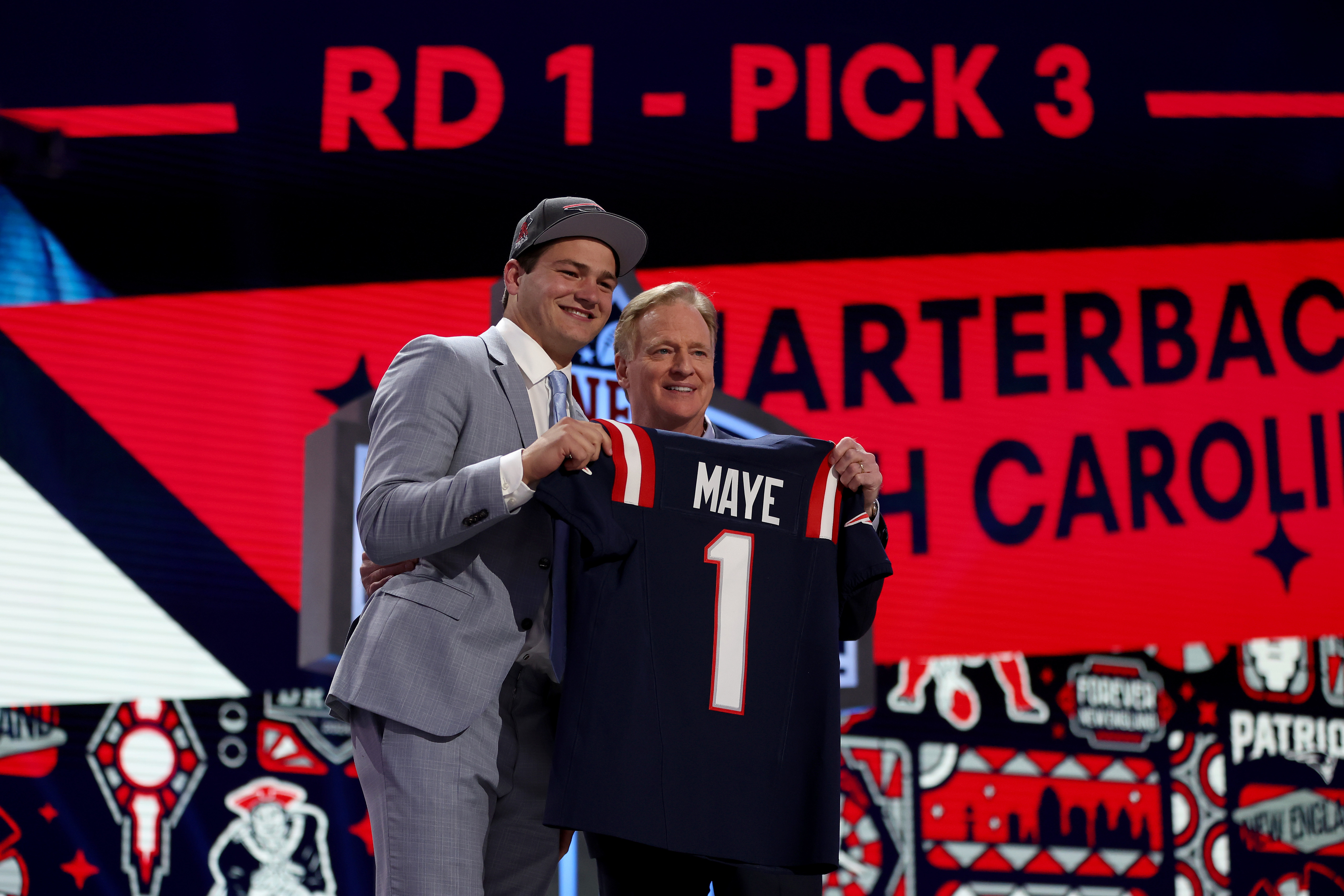 Two individuals at a sports draft event holding a jersey with the text &quot;MAYE 1&quot;