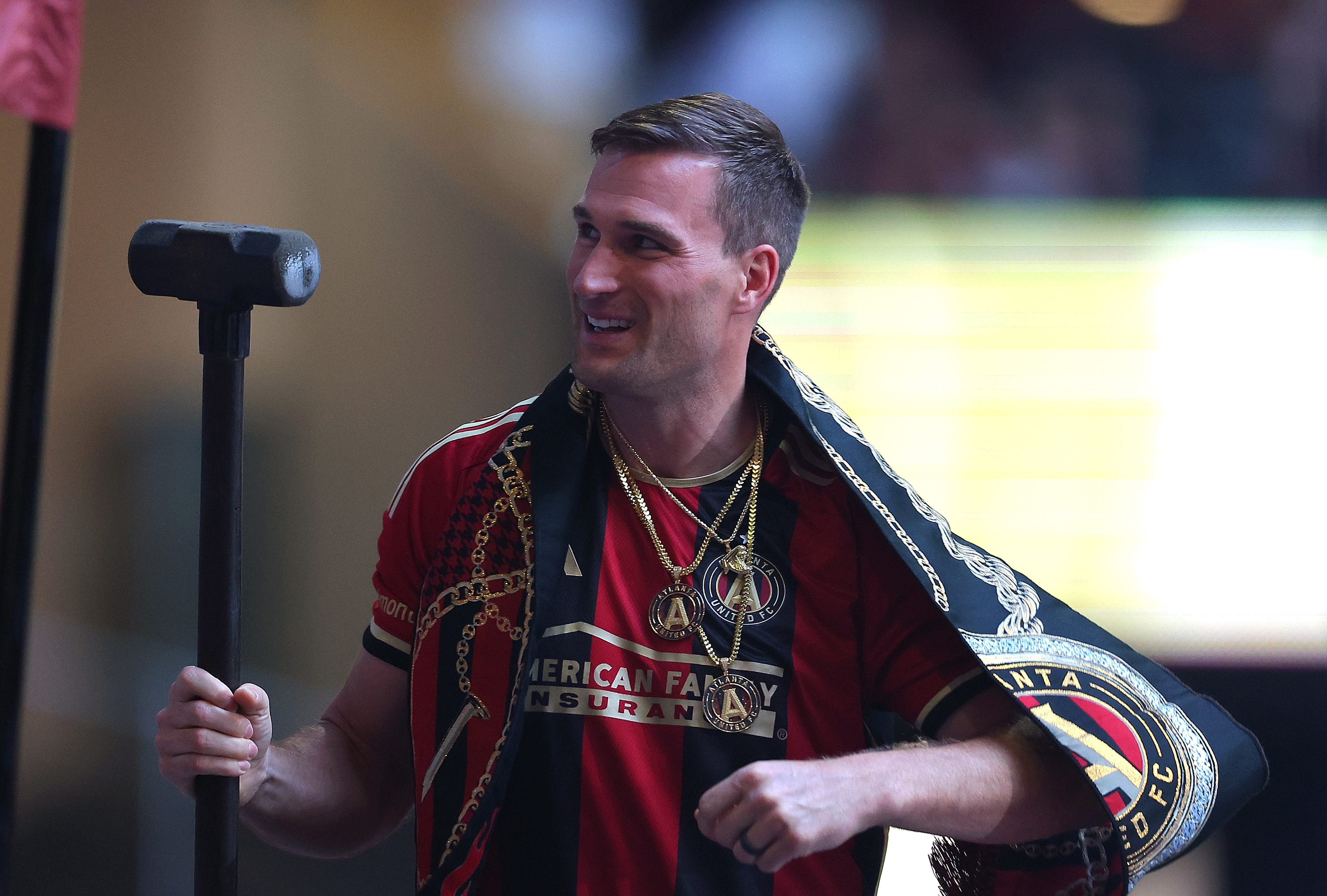 A smiling soccer player rings a bell, wearing an Atlanta United jersey with a championship medallion