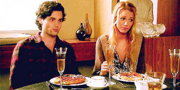 Two people at a table, one making a skeptical face, the other uncomfortable, with champagne and a waffle stack