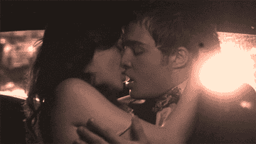 Two people sharing an intimate embrace in a dimly lit scene, creating a romantic atmosphere