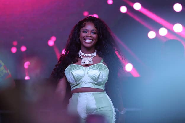 Woman smiling, performing on stage with microphone, wearing a stylish corset top and trousers. Lights in background