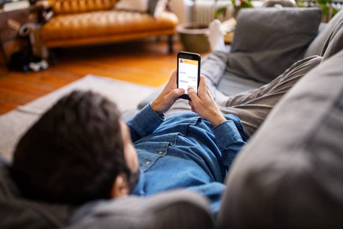 Person lying on a couch using a smartphone, viewed from over the shoulder